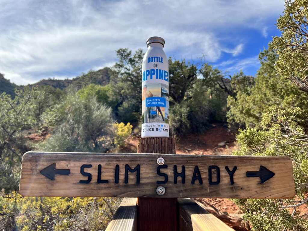 Bottle of Happiness on a Slim Shady trailhead sign symbolizing adventure with purpose in the outdoors.