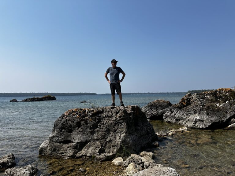 Jeremy standing confidently on a rock overlooking Lake Huron with clear blue skies