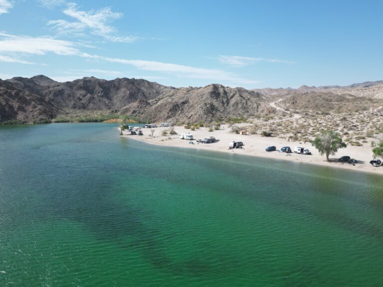 Boondocking campers lined up along the shoreline at Telephone Cove with rugged desert mountains in the background on an adventure.