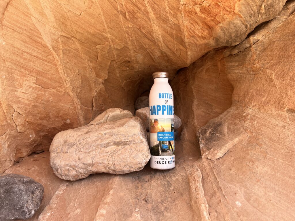 Bottle of Happiness resting on red desert rocks.
