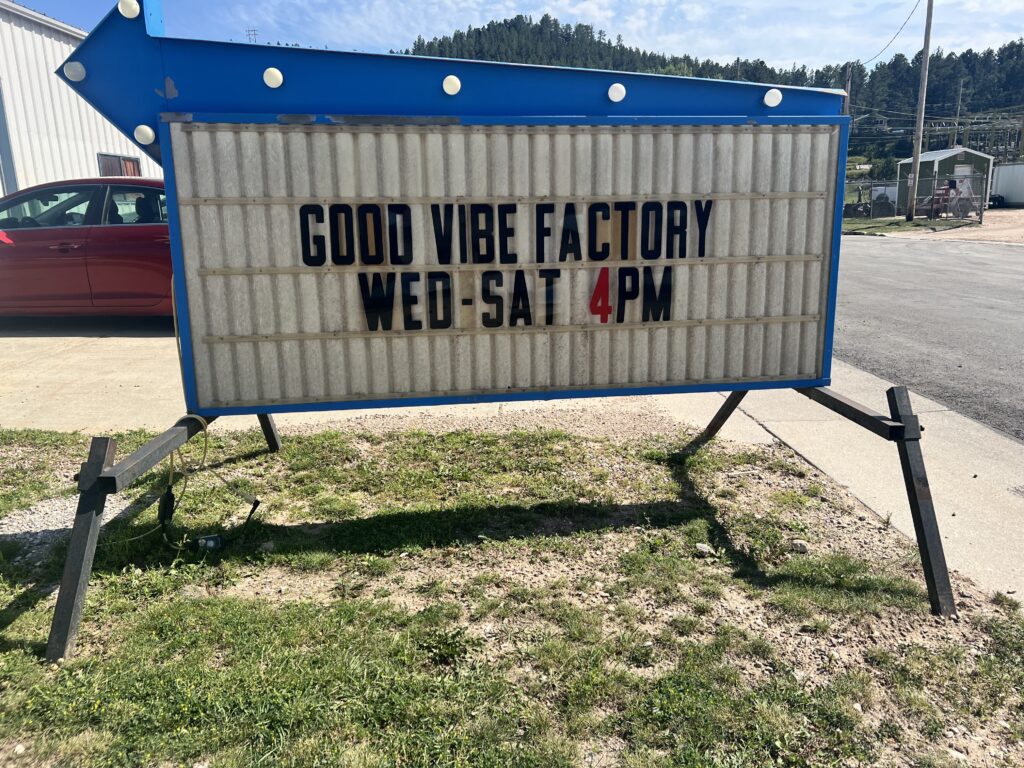 Roadside sign that reads “Good Vibe Factory Wed-Sat 4 PM.”