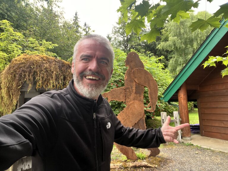 Deuce smiling in front of a rustic Bigfoot statue, symbolizing good vibes and adventure on the road.
